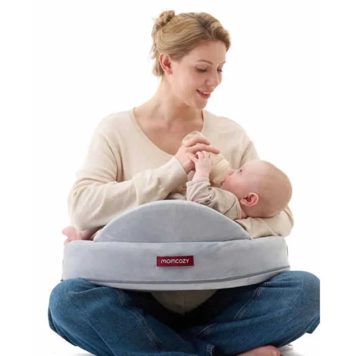 Gray U-shaped nursing pillow with Momcozy logo, supporting a baby during feeding