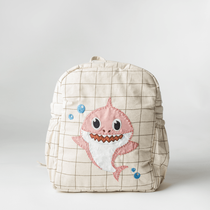 Beige check school backpack with pink shark face hand-embroidered on the front pocket.
