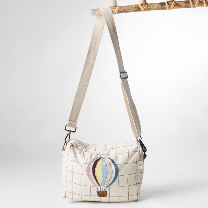 White cotton sling bag with hot air balloon patch and adjustable crossbody straps.