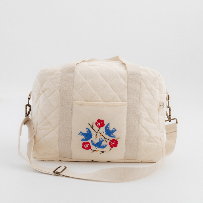 Quilted cotton nappy bag with embroidered songbirds on front panel and crossbody strap