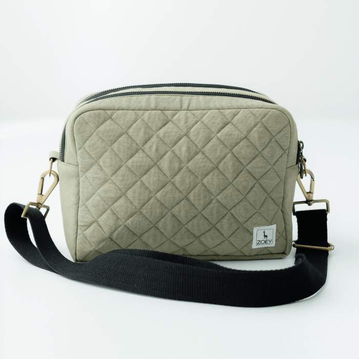 Quilted green sling nappy bag with top zipper, black crossbody strap, metal clips